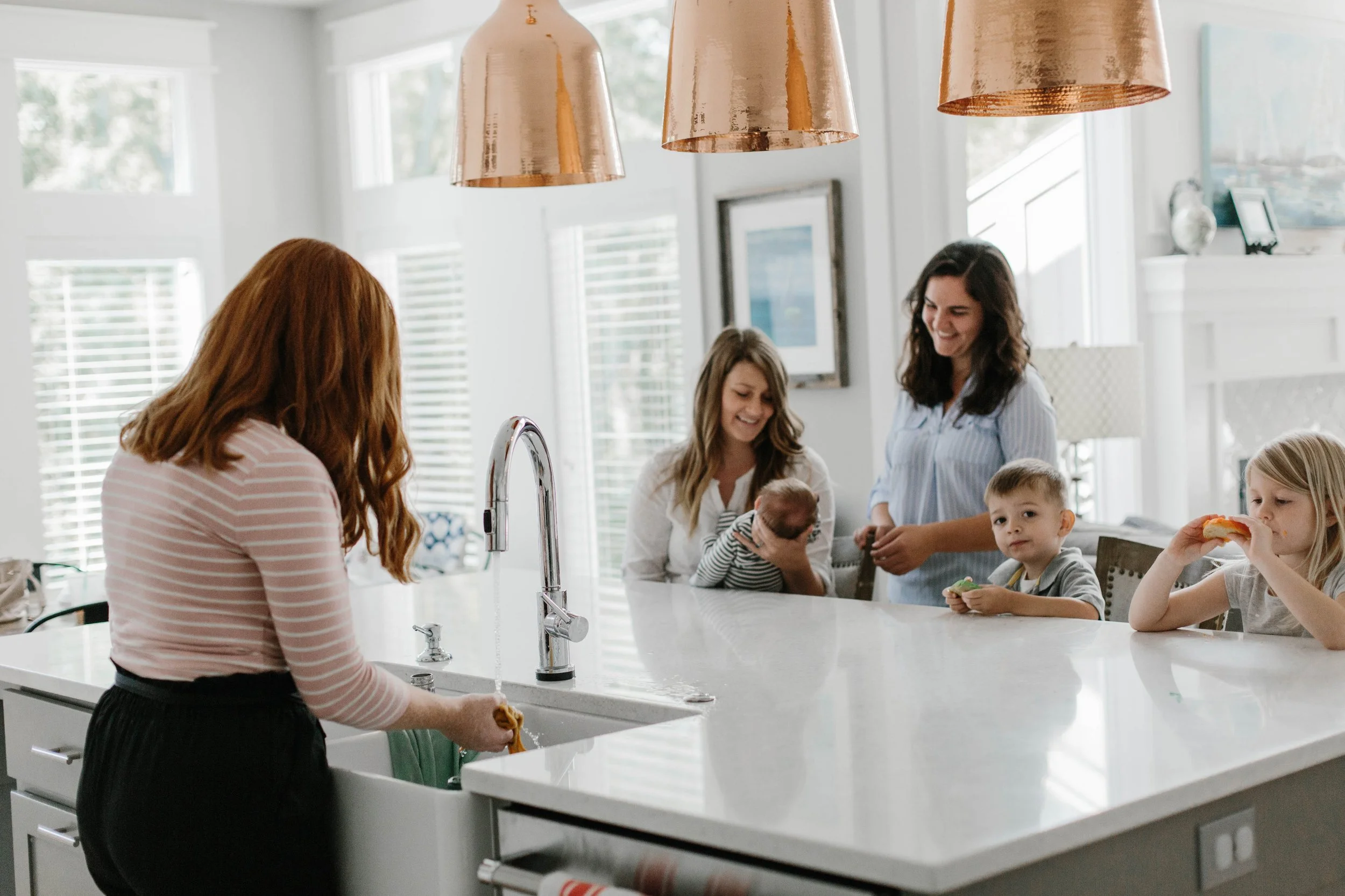 parent holding newborn near kitchen island with postpartum snacks nearby