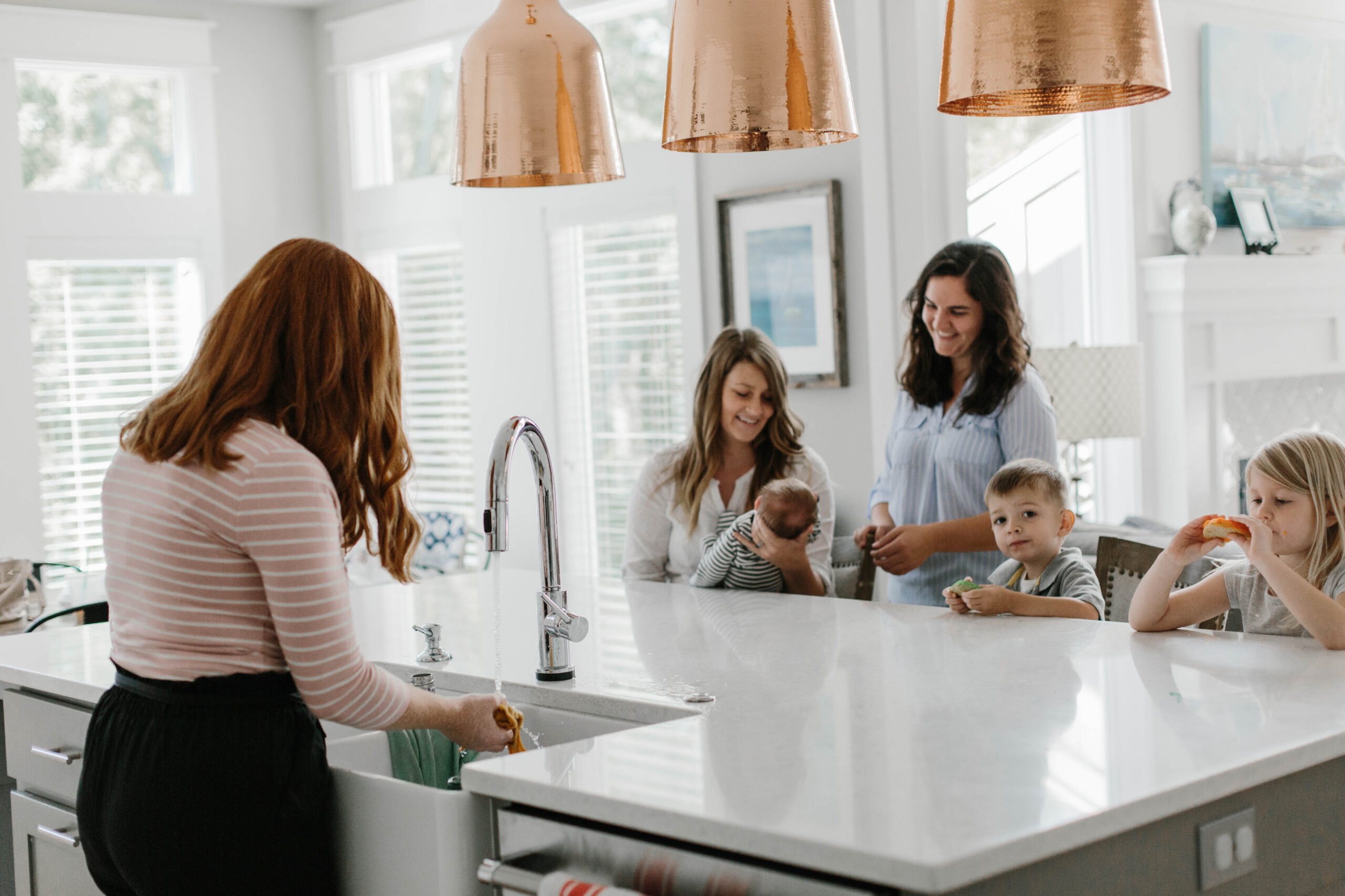 Adult holding a newborn while others gather around a bright kitchen island