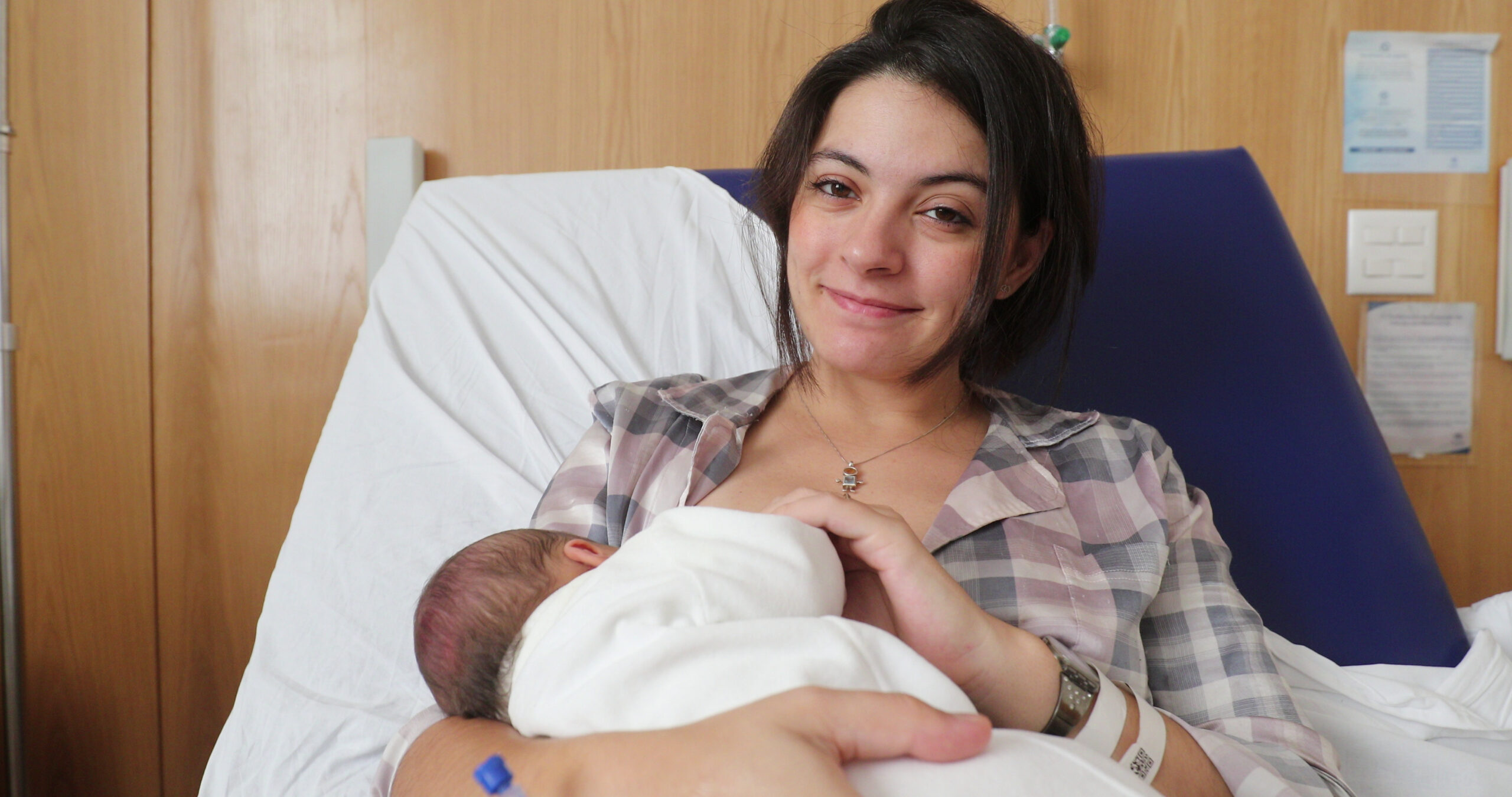 Parent sitting in hospital bed breastfeeding newborn wrapped in a white blanket