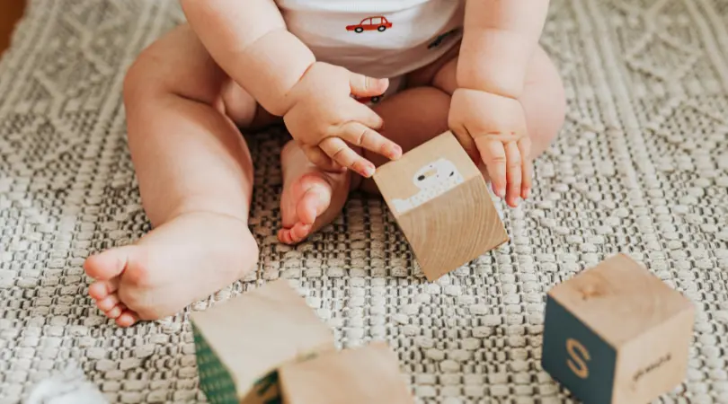 baby sitting on a soft rug exploring wooden blocks during daytime playtime