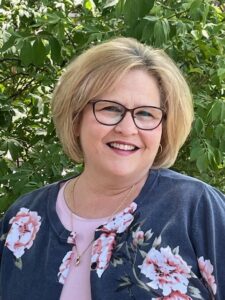caregiver wearing glasses smiling outside near leafy green trees