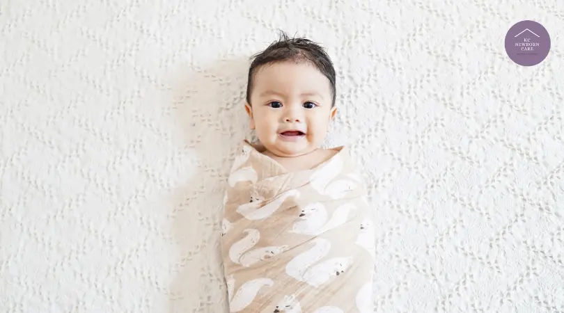 smiling newborn wrapped in a soft swaddle blanket lying on a textured white surface